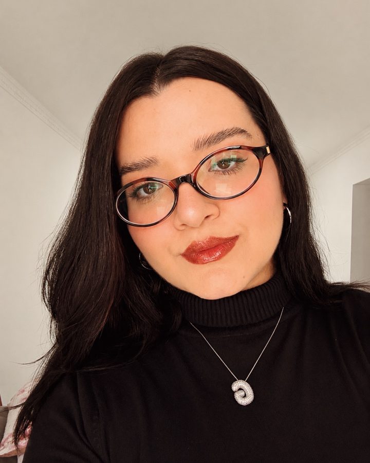Gabs, criadora da Vírgula Ideia, sorrindo de óculos e batom vinho